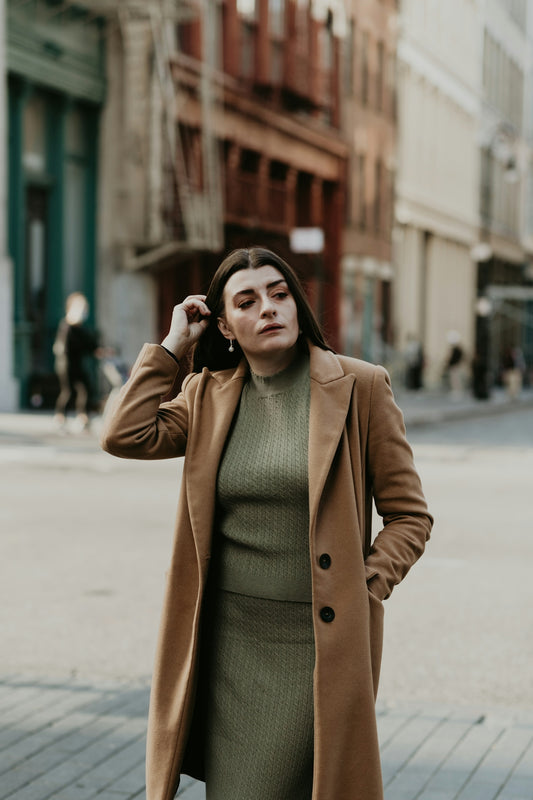 woman in brown coat standing on sidewalk during daytime