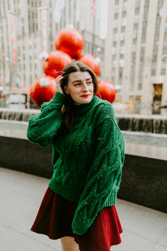 woman in green knit sweater and red skirt holding red heart balloons