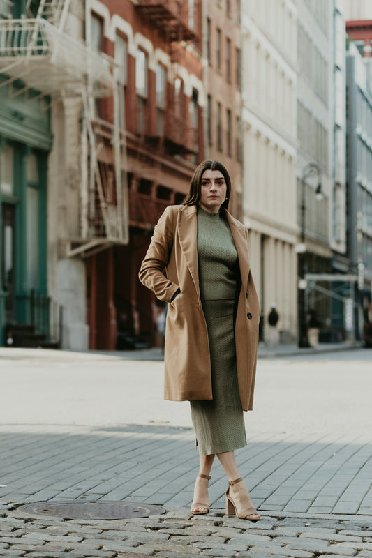 woman in brown coat standing on sidewalk during daytime
