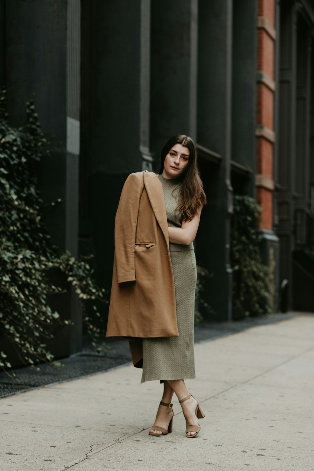 woman in brown coat standing on sidewalk during daytime